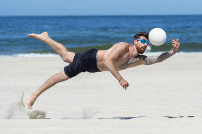 Full length of shirtless man jumping on beach