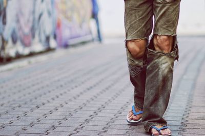Low section of man in torn pants walking on street