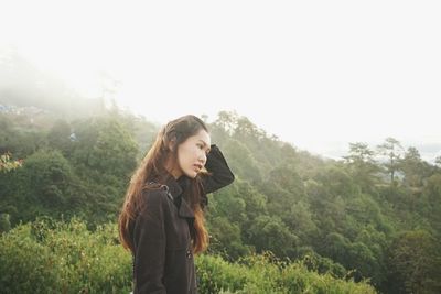 Young woman standing by tree against sky