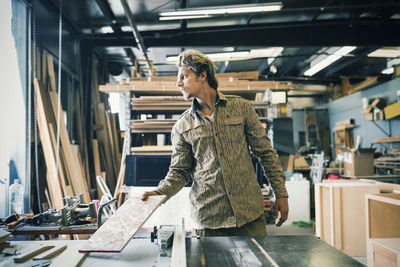 Carpenter looking away while working at table in workshop
