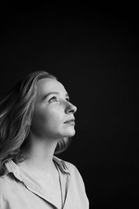 Close-up of woman looking away against black background