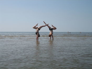 Friends doing handstand in sea against clear sky