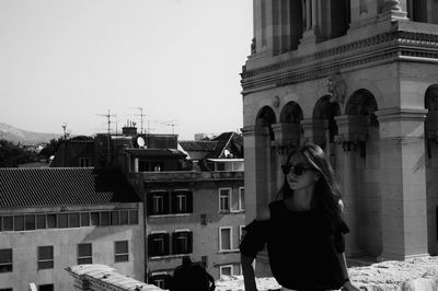 Young woman wearing sunglasses while standing on terrace against buildings