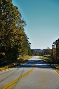 Empty road amidst trees against clear sky