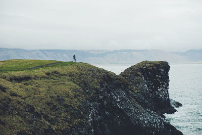 Man standing on cliff by lake against cloudy sky at snaefellsnes peninsula