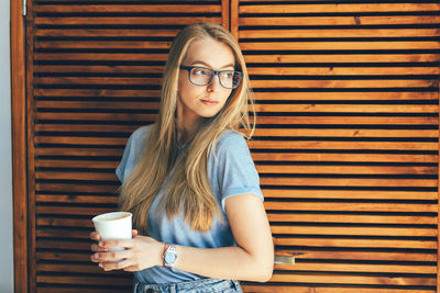 Blonde girl in glasses with a paper cup with coffee in the cafe interior. copy space for text.