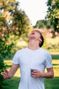 Young man looking up while standing against plants