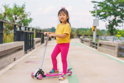 Little child girl to ride scooter in outdoor sports ground on sunny summer day. 