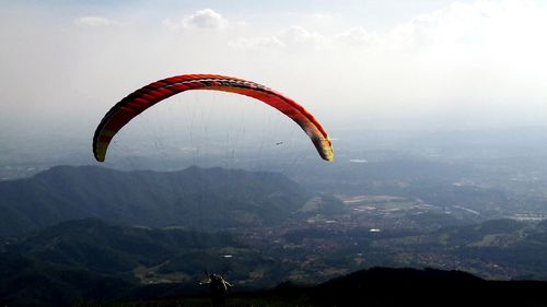 Person paragliding over mountains against sky