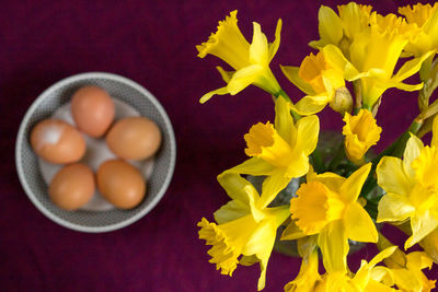 High angle view of yellow daffodils with eggs in bowl on table