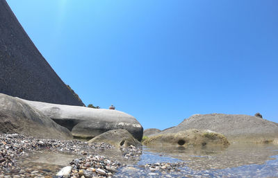 Rocks by sea against clear blue sky