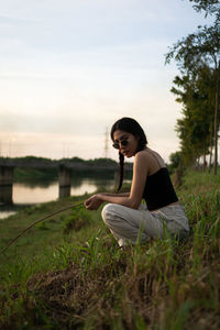 Side view of woman sitting on field against sky during sunset