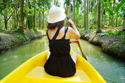 Rear view of woman wearing hat by lake in forest