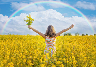 Rear view of girl holding flower with arms raised standing in field