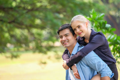 Smiling man carrying woman on back in park