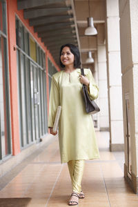 Thoughtful woman holding purse while standing in corridor