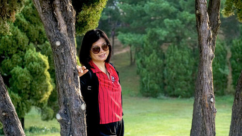 Portrait of smiling young woman standing on tree trunk in forest