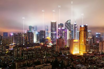 Illuminated modern buildings in city against sky at night