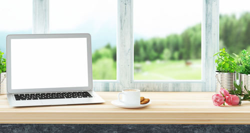 Close-up of laptop and breakfast on table by window