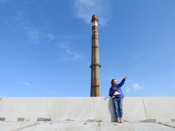 Low angle view of woman pointing while standing by lighthouse against sky