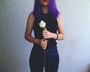 Midsection of young woman holding flower while standing against wall