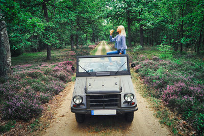 Woman holding bottle while standing in jeep at forest