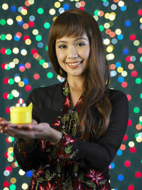 Portrait of woman with oil lamp against illuminated lights