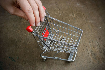 Cropped hand of person holding miniature shopping cart on wooden table