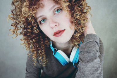 Portrait of woman with curly hair wearing headphones against wall