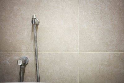 Close up of chrome faucet and shower in on a background of tiled wall in the bathroom.