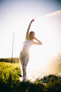 Young woman with arms raised on field against sky