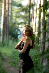 Young woman standing by tree in forest