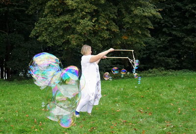 Smiling woman making bubbles while standing against trees
