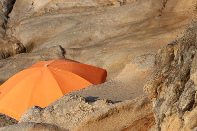 Orange parason sunshade hiding between stones 