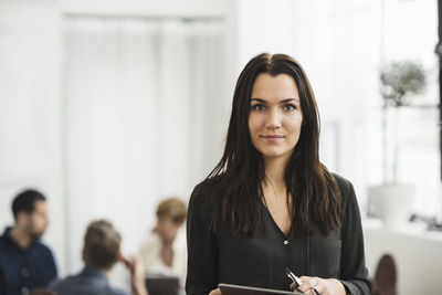 Portrait of businesswoman standing with people in background