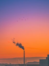 Silhouette smoke emitting from chimney against sky during sunset