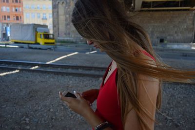 Side view of young woman using mobile phone while standing by railroad track