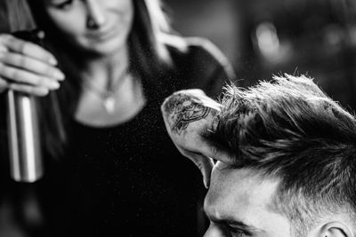 Close-up of woman spraying on man hair at shop