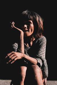 Portrait of woman sitting against black background