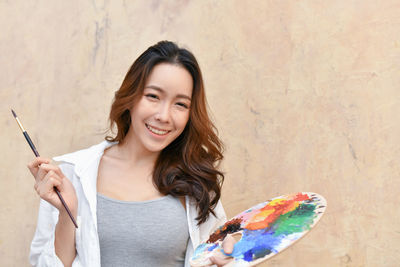 Young woman holding colorful palate against wall