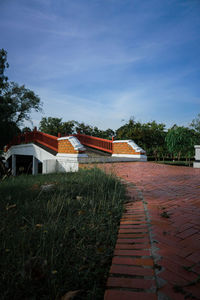 Footpath amidst houses and trees against blue sky