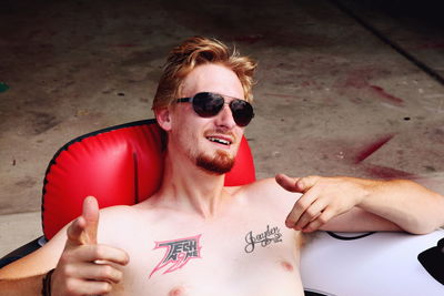 Portrait of shirtless man wearing sunglass on seat