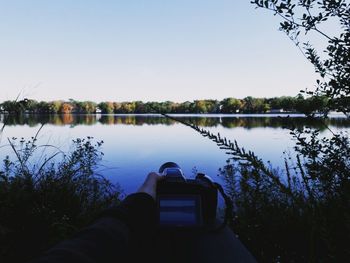 Close-up of hand by lake against clear sky