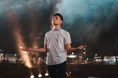 Young man looking away while standing at night