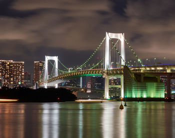 Illuminated bridge over river in city at night