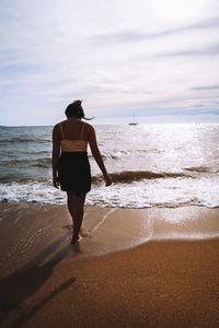 Rear view of man standing on beach against sky