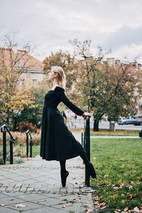 Ballerina dancing in autumn city street, modern ballet dancer in black dress, pointe shoes outdoors