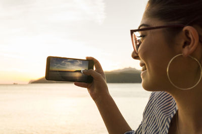 Close-up of teenage girl photographing sunset through smart phone