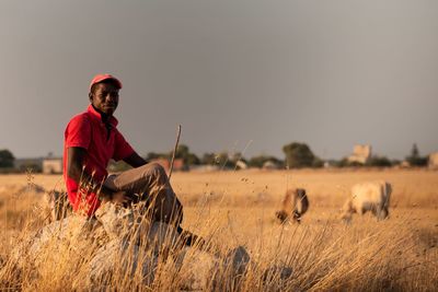 Full length of man sitting on field against sky
