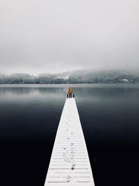 Rear view of person standing on pier over lake against sky during winter